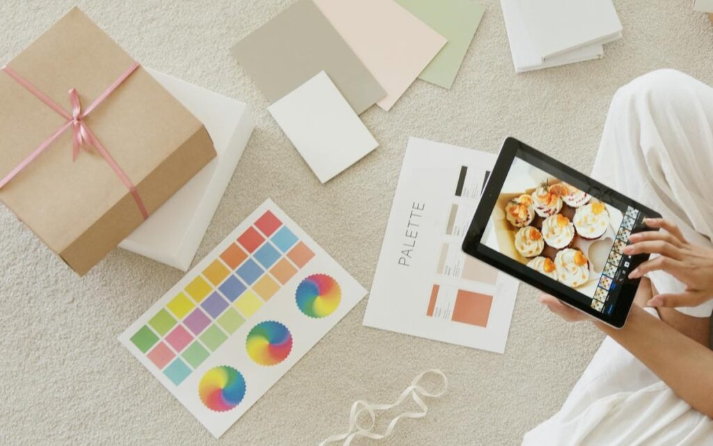 Dein All-in-One Guide – Alles rund um Branding 1 Eine Person wählt zwischen Fotos auf einem Tablet und Farbproben auf Papier auf dem Boden aus