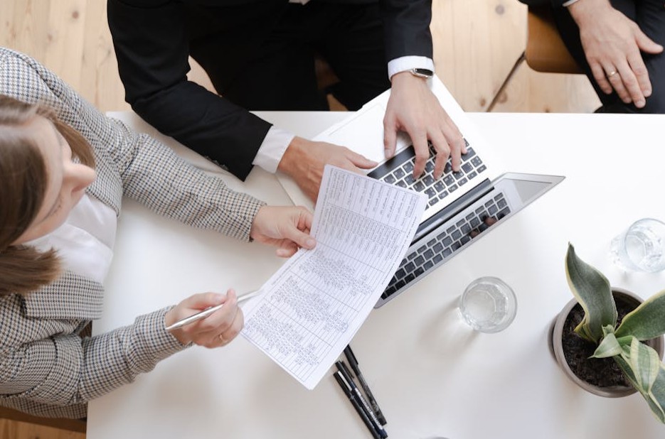 Employer Branding: Definition, Best Practices, Maßnahmen 4 Drei Personen besprechen ein Dokument, ein Laptop steht auf dem Tisch, auf dem mitgeschrieben wird