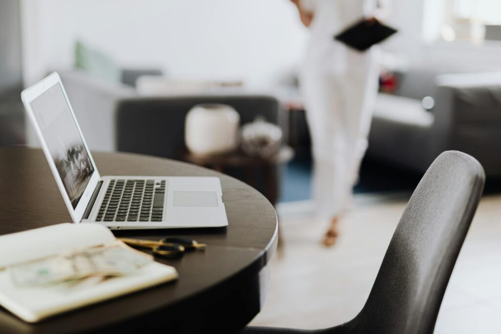 Branchenverzeichnisse für SEO & Sichtbarkeit 4 Laptop auf einem Tisch im Fokus, im Hintergrund unscharf eine Person, die mit einem Notizblock Richtung Kamera kommt